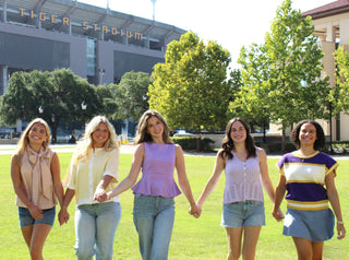 Women wearing purple and gold LSU game day outfits near Tiger Stadium