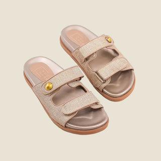 Pair of beige sandals with gold buckles on a light gray background