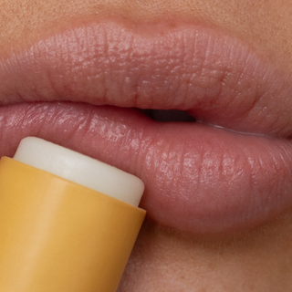 Close-up of a person applying yellow lip balm to their lips.