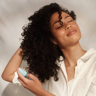 Woman with curly hair holding a blue bottle against a neutral background