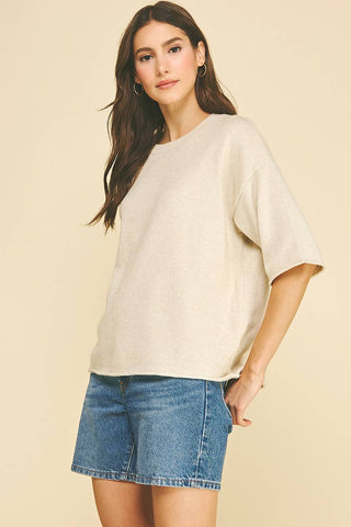 Woman wearing a beige top and blue denim shorts against a beige background