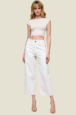 Woman wearing a white crop top and white pants against a plain background