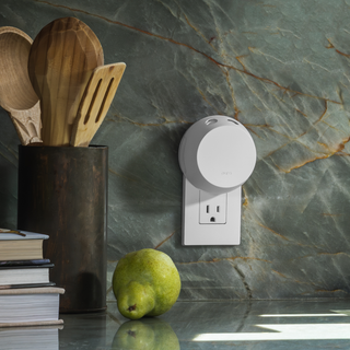pure Smart plug on a marble countertop with wooden utensils, books, and a pear.