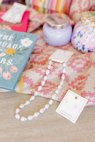 Pearl necklace with a tag on a textured surface with a book and decorative items in the background.