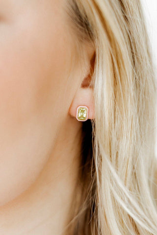 Close-up of a person wearing a green gemstone earring with blonde hair.