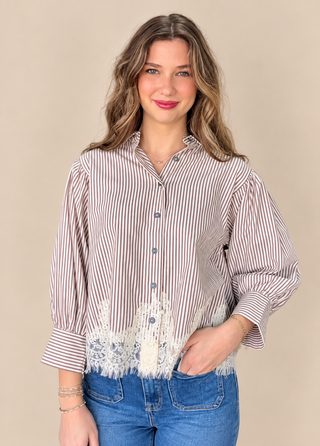 A woman wearing a brown and white vertically striped button-down blouse with white lace trim at the hem, paired with blue jeans, against a solid beige background.