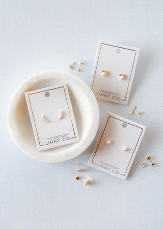 Gold earrings on LINNY CO cards with a marble dish on a light gray background