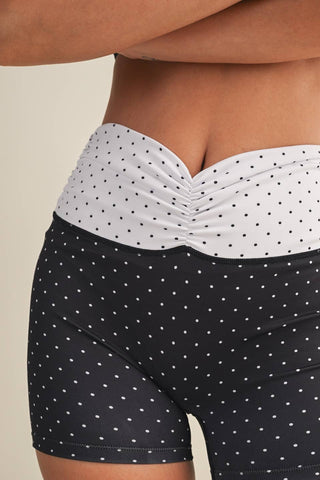 Person wearing black polka dot shorts with a white top on a beige background