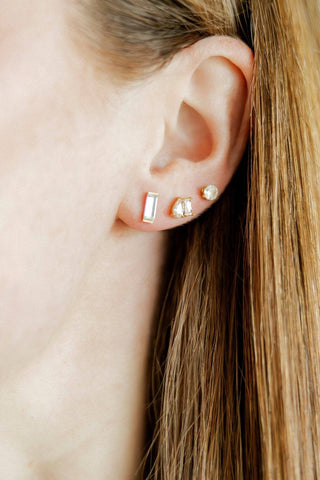 Close-up of an ear wearing gold stud earrings with a blurred background