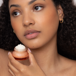Woman holding a small container of cream close to her face