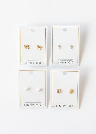 Four pairs of gold earrings on LINNY CO cards against a white background
