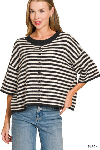 A woman wearing a black and off-white striped knit poncho cardigan with a button front, paired with blue jeans, against a plain white background.