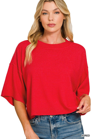 A woman wearing a bright red knit short-sleeve top with wide batwing sleeves and blue jeans, shown against a plain white background.