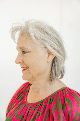 Woman with gray hair wearing a pink and green patterned top against a white background