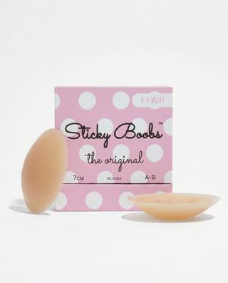 A pink polka-dot box labeled 'Sticky Boobs the original' with two flesh-toned adhesive nipple covers placed in front on a clean white background.
