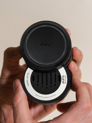 Black Pura candle diffuser held by hands against a beige background
