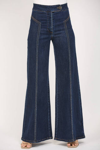 Dark blue wide-leg denim jeans with prominent contrast light-colored stitching running down the front of the legs, shown on a model wearing beige flat sandals against a plain white studio background.
