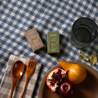 Table setting with pomegranate, pear, plums, wooden spoon and fork on a checkered tablecloth.