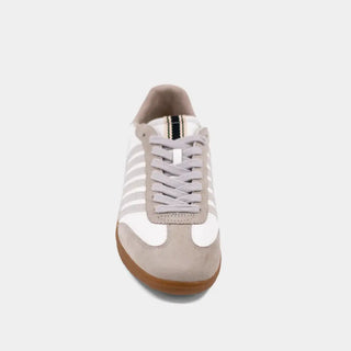 Sneaker with white laces and a brown sole on a light gray background