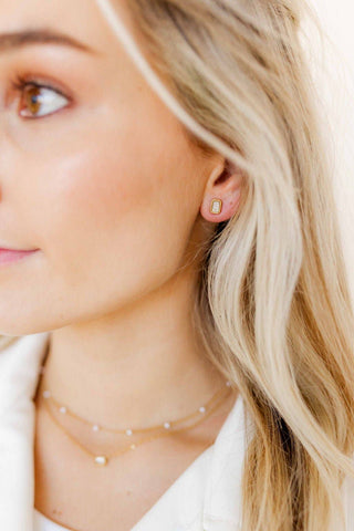 Close-up of a woman wearing gold earrings and necklaces with a neutral background
