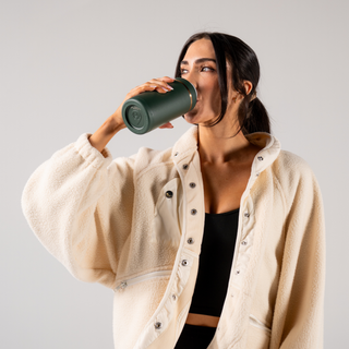 Woman drinking from a green thermos against a plain background