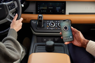 Person using a smartphone with a car's infotainment system displayed on the screen.