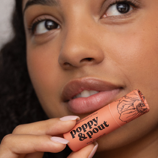 Close-up of a person holding a 'Poppy & Pout' product near their lips.