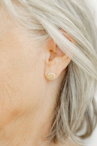 Close-up of an ear wearing a small gold earring with a clear gemstone.