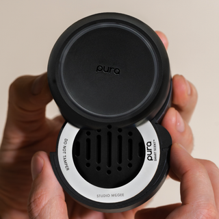 Pura smart scent diffuser held by a hand with a neutral background