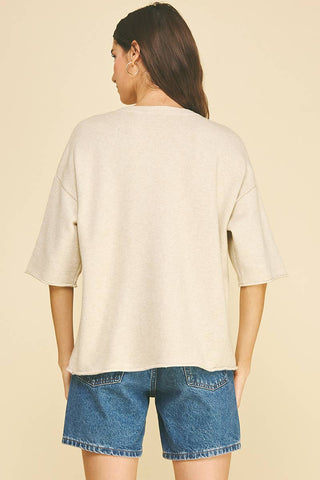 A woman shown from the back wearing an oversized cream-colored short-sleeve top and blue denim shorts against a solid beige background.