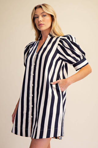 A woman modeling a short puff-sleeve shirt dress with vertical navy and white stripes, set against a plain beige studio background.