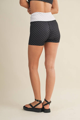 Person wearing black polka dot shorts on a beige background