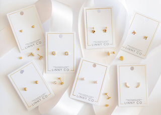 Gold earrings on LINNY CO display cards against a white background