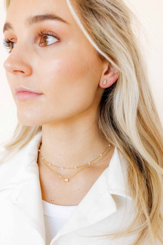 Close-up of a woman wearing gold necklaces and earrings against a neutral background