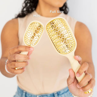 Person holding a mini and full-size hairbrush with gold bristle patterns.