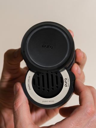 Person holding a black and silver Pura product against a beige background
