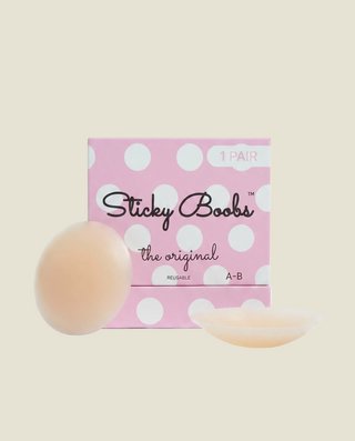 A pink polka-dot box labeled 'Sticky Boobs the original' with two pale flesh-toned reusable adhesive breast pads shown in front on a light beige background.