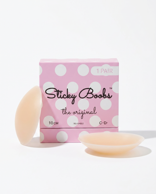 A pink polka-dot box labeled 'Sticky Boobs the original' with two pale peach silicone breast-shaped stickers placed in front on a clean white background.