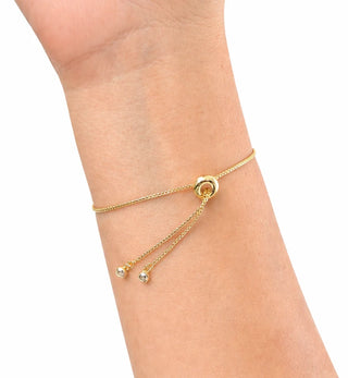 A delicate gold chain bracelet with a central ring and two dangling bead chains, shown worn on a person's wrist against a plain white background.