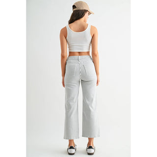 Woman wearing a white sleeveless top and striped pants with a beige cap on a white background