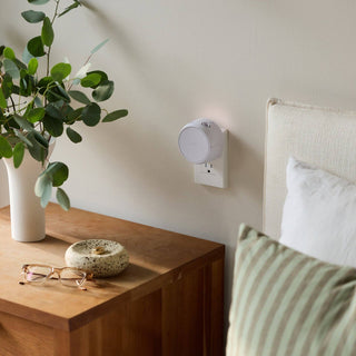 Pura smart fragrance diffuser plugged in by a bed