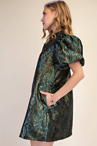 A woman wearing a short puff-sleeve dress with a dark green and black marbled pattern, photographed against a plain beige studio background.