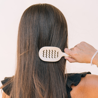 Person using a hairbrush on their long hair with a plain background