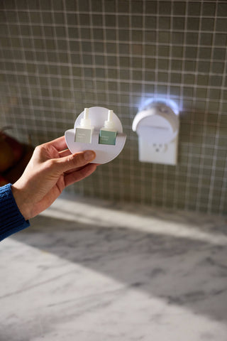 Hand holding a small round product with a blurred bathroom background