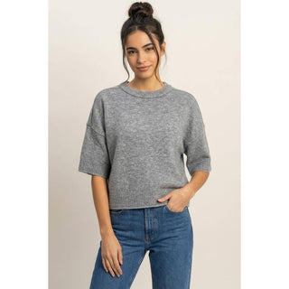 Woman wearing a gray sweater and blue jeans on a plain background