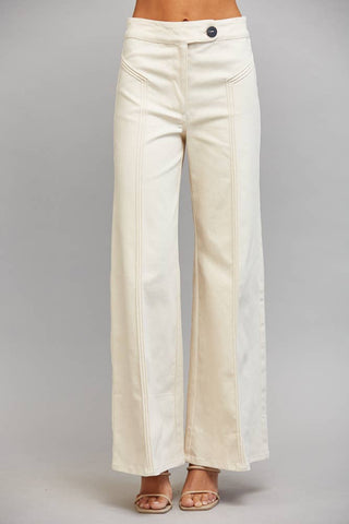 A model from the waist down wearing off-white wide-leg pants with vertical seam detailing down the front of the legs, paired with metallic sandals, against a neutral gray background.