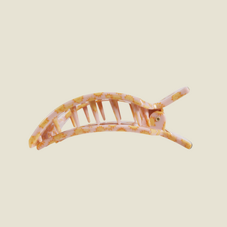 A curved claw-style hair clip in a translucent pink resin with a yellow floral pattern, shown against a solid light beige background.