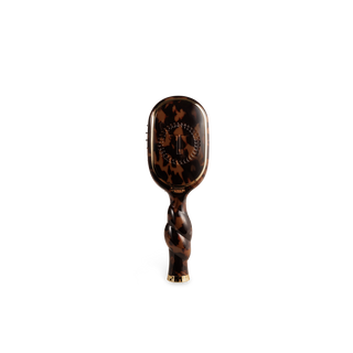 A hairbrush with a glossy tortoiseshell pattern handle and head, featuring a twisted grip and gold-tone metal accents at the base, shown against a plain white background.