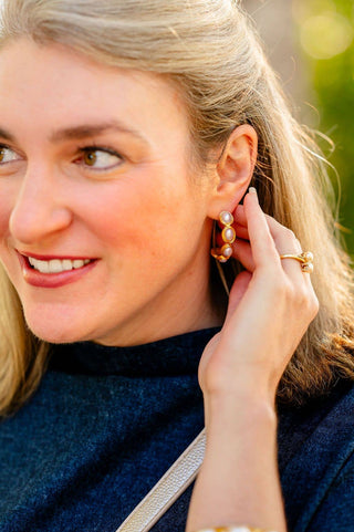 Woman wearing pearl earrings and a gold ring, with a blurred natural background