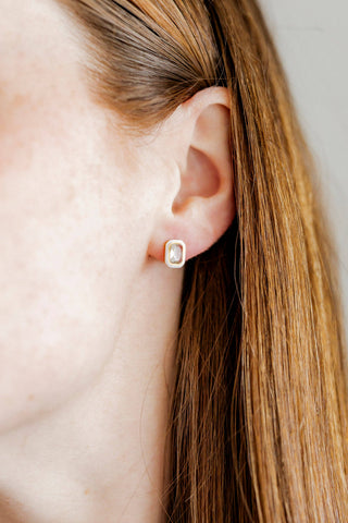 Close-up of an ear wearing a gold earring with a clear gemstone.